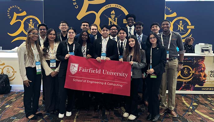 Image of a group of Fairfield University students poses for a photo holding a banner