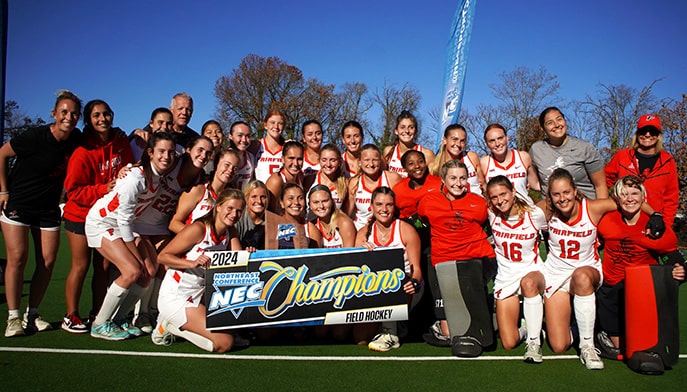 Female field hockey student-athletes smiling in a group photo while holding up their 2024 NEC Champions baner.